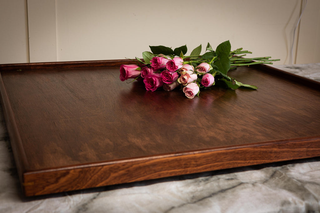 Wooden tray with a bouquet of pink and white roses on a marble surface.